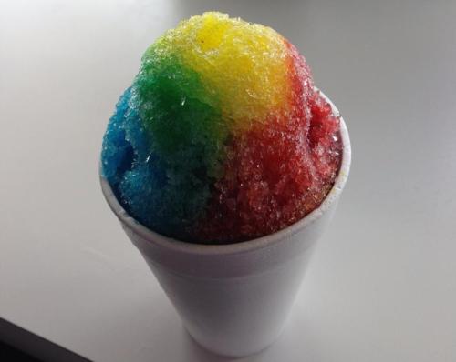 A colorful snow cone with blue, green, yellow, and red layers, served in a white cup.