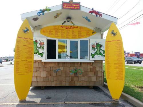 A colorful food kiosk with a surfboard design, featuring a menu and tropical decorations.