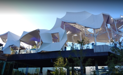 Modern architectural building with flowing white canopies and a glass base, surrounded by greenery.