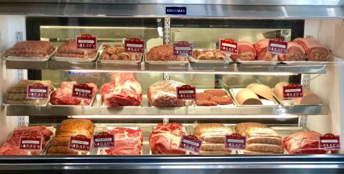 A display case filled with various meats, including sausages, ground meat, and cuts of beef, all labeled for sale.