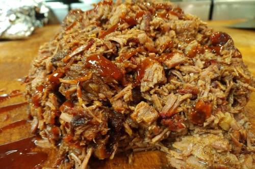 A close-up of shredded barbecue beef topped with sauce, resting on a wooden cutting board.