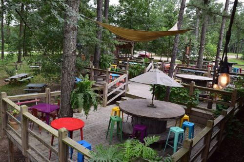 A vibrant outdoor seating area with colorful tables and chairs surrounded by trees and greenery.