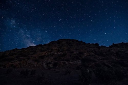 A starry night sky over a dark, rugged mountain silhouette. The Milky Way is faintly visible among the stars.