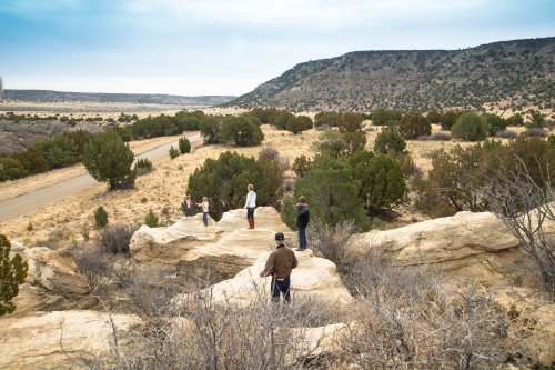 A group of people standing on rocky terrain, overlooking a vast, dry landscape with sparse vegetation and distant hills.