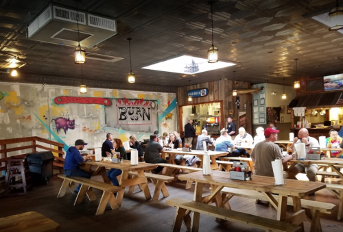 A rustic restaurant interior with wooden tables, patrons dining, and colorful murals on the walls.