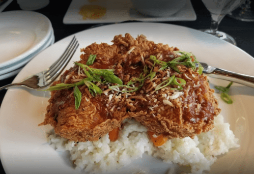 A plate of fried chicken topped with sauce and green onions, served over a bed of rice.