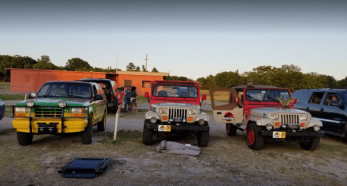 Three colorful SUVs parked in a grassy area, with people gathered in the background and a building behind them.