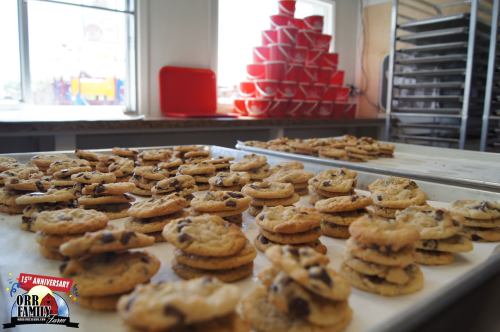 A tray of freshly baked chocolate chip cookies, with a stack of red cups in the background.