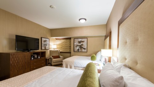 A cozy hotel room featuring two beds, a TV, and modern decor with warm tones and soft lighting.