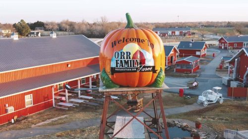 A large pumpkin sign welcomes visitors to Orr Family Farm, surrounded by red barns and outdoor seating.