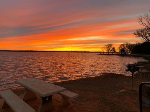 A serene lakeside scene at sunset, featuring vibrant orange and purple skies, with a picnic table in the foreground.