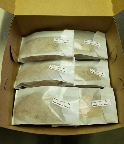A box containing several individually wrapped apple pies with labels on each package.
