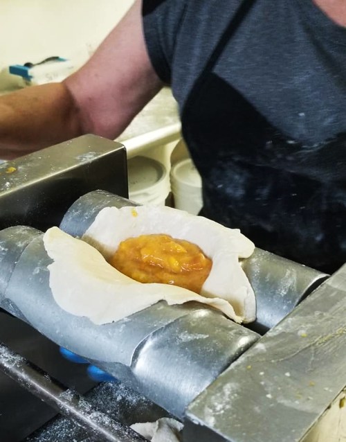 A person is filling a dough wrapper with a yellow filling using a machine in a kitchen setting.