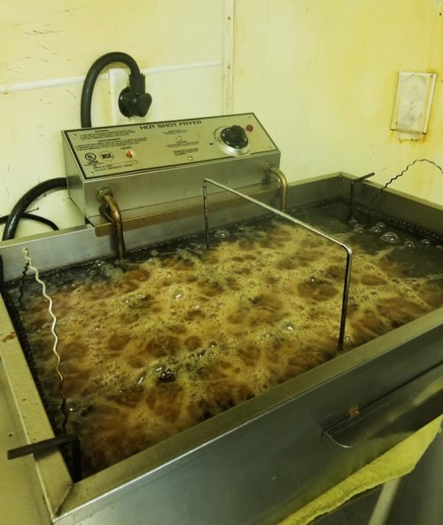A deep fryer filled with bubbling oil, with a temperature control panel and a metal rack inside.