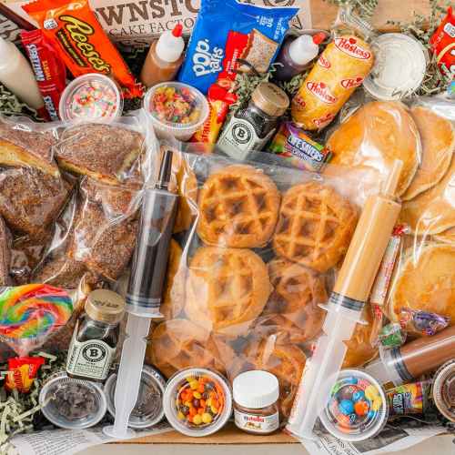 A variety of sweet treats including waffles, pancakes, candies, syrups, and toppings arranged in a festive box.