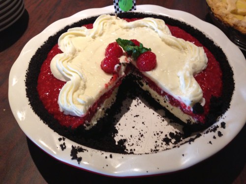 A sliced dessert with a chocolate crust, layered with raspberry filling, whipped cream, and topped with raspberries.