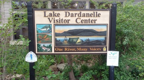 Sign for Lake Dardanelle Visitor Center featuring wildlife illustrations and the phrase "One River, Many Voices."