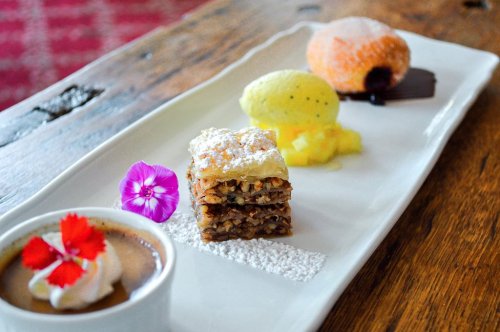 A dessert plate featuring baklava, ice cream, a colorful pastry, and a cup of coffee with whipped cream and a flower garnish.