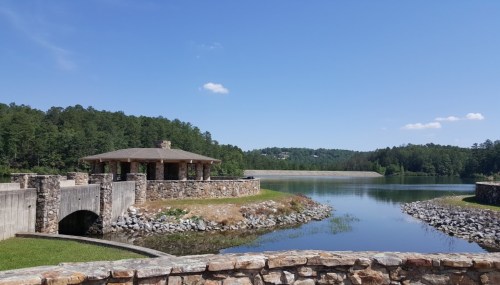 A serene lake view with a stone pavilion and lush green trees under a clear blue sky.