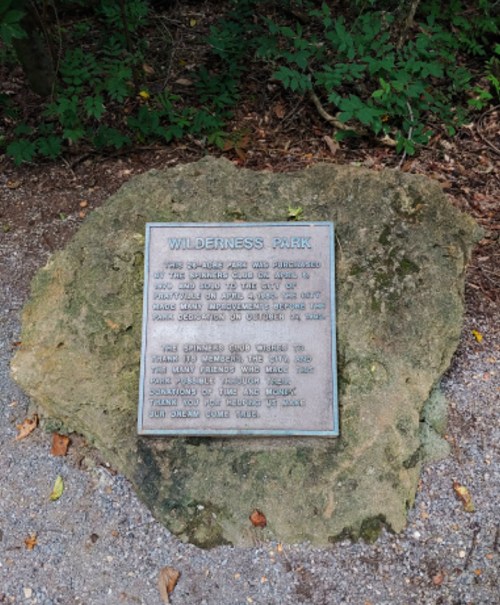 A plaque on a rock at Wilderness Park, detailing park history and visitor guidelines. Surrounded by gravel and trees.