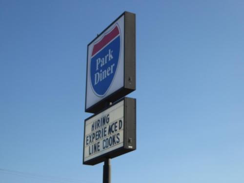 Sign for Park Diner with a message: "Hiring Experienced Line Cooks" against a clear blue sky.