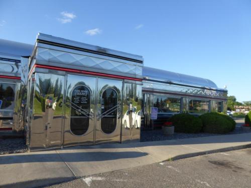 A shiny, silver diner exterior with large glass doors and a landscaped entrance on a sunny day.