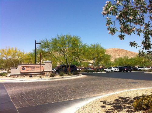 Entrance to Exploration Peak Park, featuring desert landscaping, a sign, and parked cars under a clear blue sky.