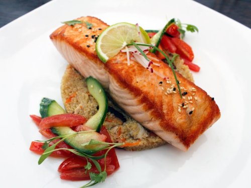 Grilled salmon fillet with lime, served on quinoa and garnished with fresh vegetables and herbs.