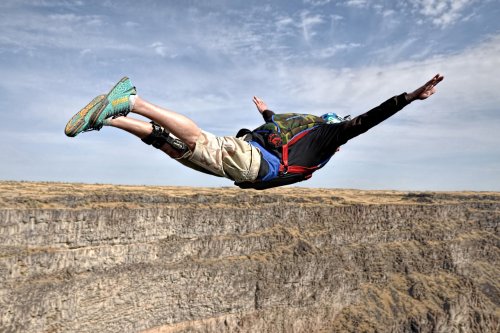 A person in a black shirt and shorts is skydiving over a rocky canyon, arms outstretched and legs extended.