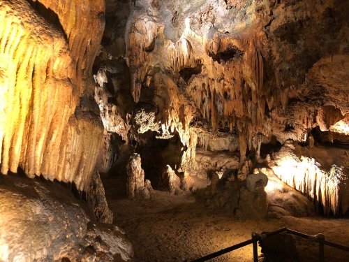 A dimly lit cave interior featuring stalactites and stalagmites, with warm lighting highlighting the rock formations.