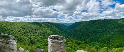 A panoramic view of a lush green valley surrounded by hills under a partly cloudy sky.