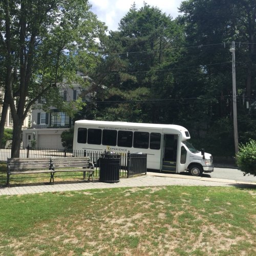 A white shuttle bus parked near a grassy area with benches and trees, in a residential neighborhood.