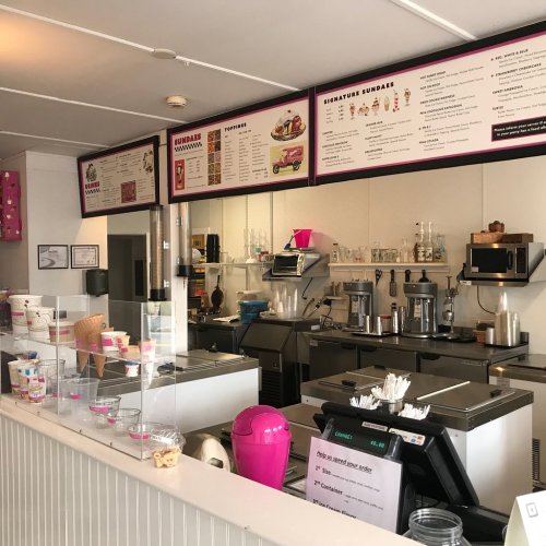 Interior of an ice cream shop featuring a service counter, menu board, and various ice cream supplies.