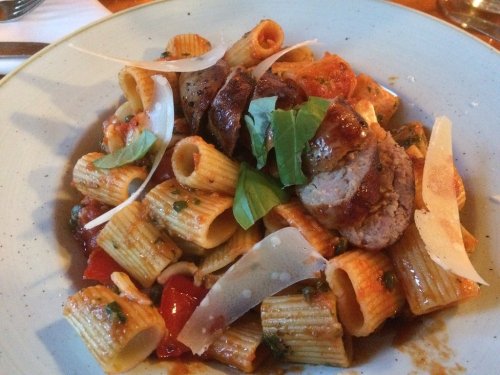 A plate of rigatoni pasta topped with sausage, tomato sauce, basil, and shaved cheese.