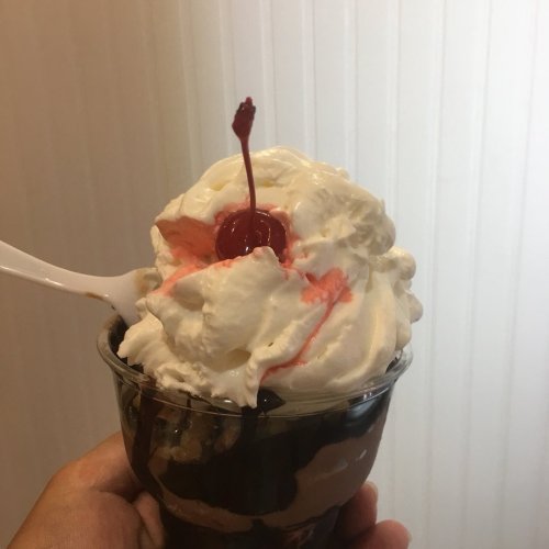 A hand holding a dessert cup filled with chocolate ice cream, topped with whipped cream and a cherry.