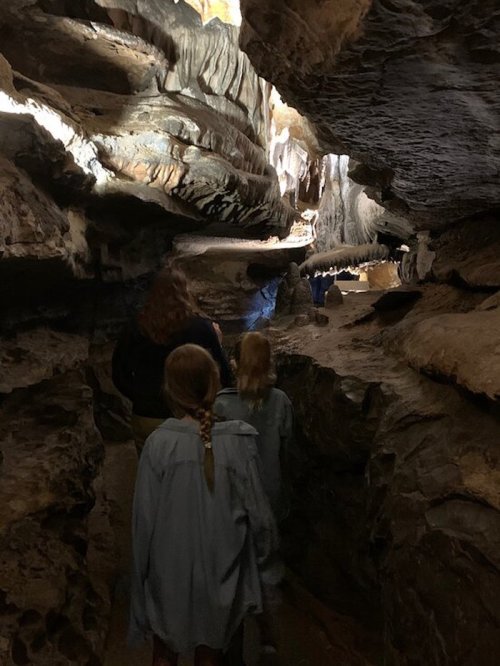 Two children and an adult walk through a narrow cave passage, illuminated by soft light from above.