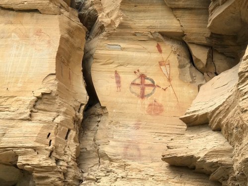 Ancient rock art featuring red and ochre symbols on a textured sandstone surface.