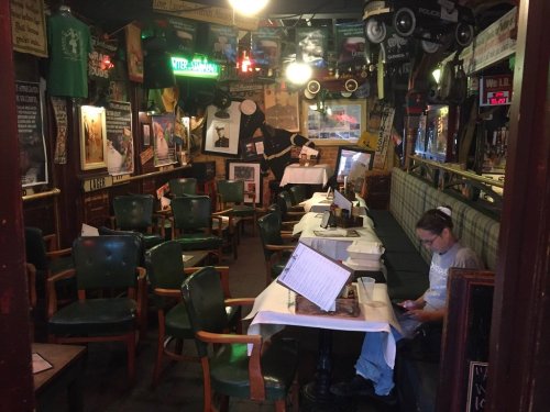 A cozy pub interior with empty tables, green chairs, and vintage decor, featuring a person sitting and using a phone.