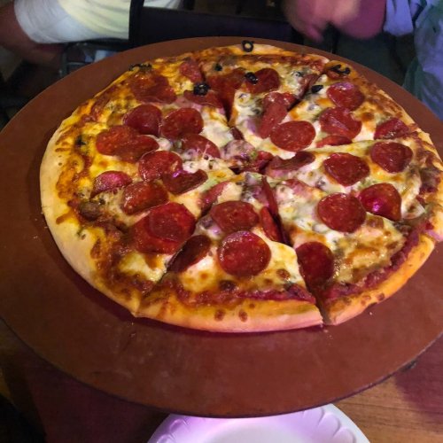 A freshly baked pepperoni pizza on a wooden serving board, sliced into eight pieces, with black olives on top.