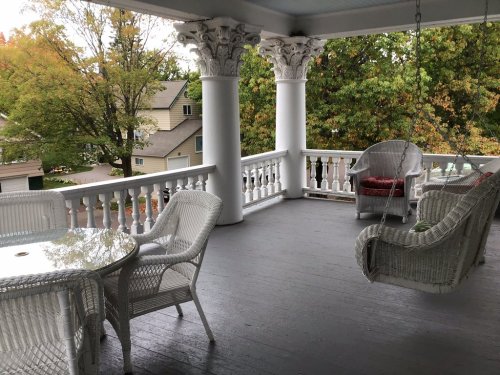 A spacious porch with white wicker furniture, columns, and colorful autumn trees in the background.