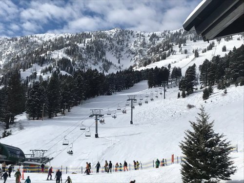 Ski resort scene with snow-covered slopes, ski lifts, and people enjoying winter activities under a cloudy sky.