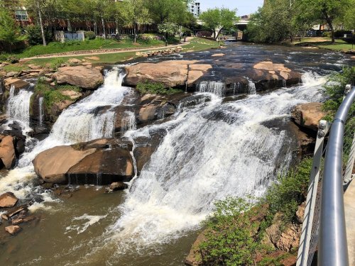 A scenic view of a waterfall cascading over rocks, surrounded by greenery and a peaceful riverbank.