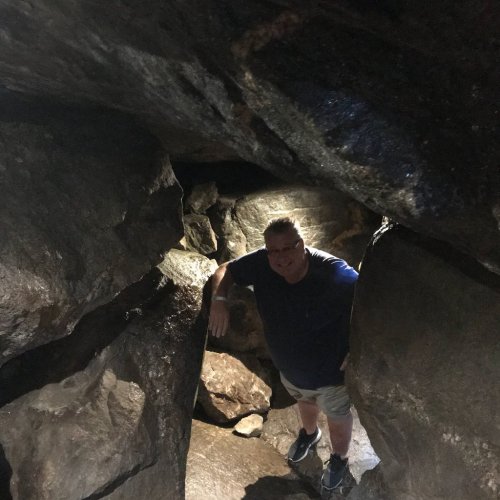 A person stands between large rocks in a cave, smiling and leaning against the stone wall.