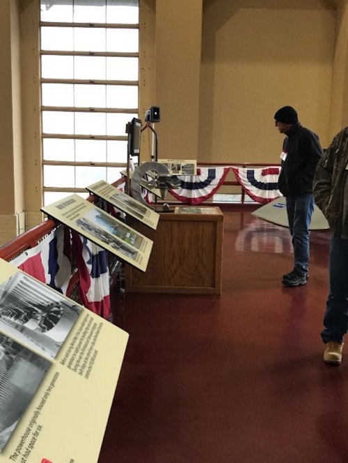 A museum exhibit with informational panels and a visitor observing the displays, decorated with red, white, and blue bunting.