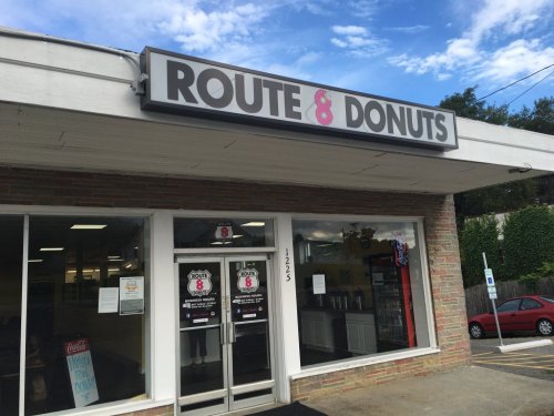 Exterior of Route 8 Donuts shop with a sign, large windows, and a clear blue sky above.