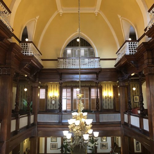 Interior of a grand building featuring wooden pillars, a chandelier, and arched ceilings with balconies above.
