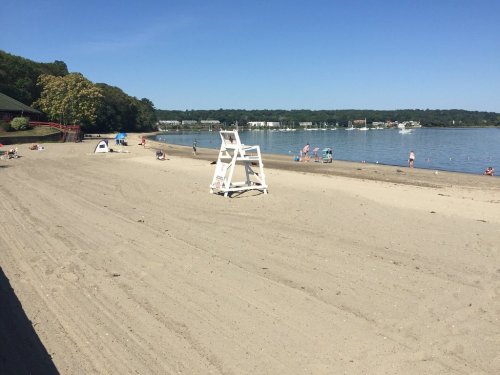 A sandy beach with a lifeguard chair, people sunbathing, and calm water under a clear blue sky.