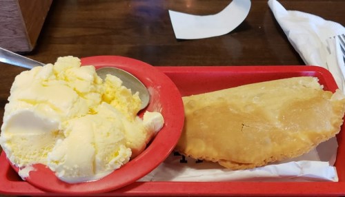 A red tray holds a bowl of yellow ice cream and a golden-brown fried pastry on a napkin.