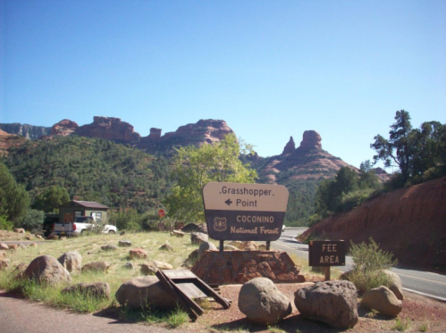 Sign for Grasshopper Point in Coconino National Forest, with rocky hills and clear blue sky in the background.