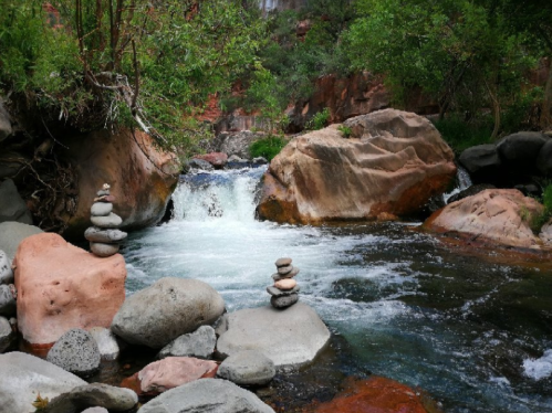 A serene river scene with stacked stones, flowing water, and lush greenery on either side.